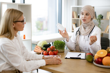 Muslim doctor in hijab receives female patient in modern clinic. Happy pretty Arabian female...