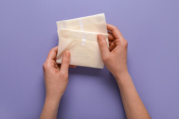 Female hands with menstrual pads on purple background