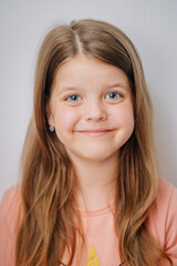 Fototapeta premium A smiling young girl with long brown hair and blue eyes, wearing a peach-colored shirt and small heart-shaped earrings...