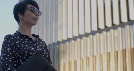 Portrait of a woman, expert business coach, standing in sunglasses against the backdrop of a modern building. Concept of professional coaching, business expertise, and urban lifestyle. Space for text.
