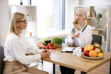 Professional nutritionist talks to patient about benefits of healthy diet while holding avocado....