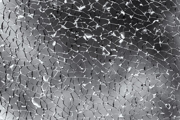 Close-up of glass covered with many cracks. Divided into a large number of pieces. Gray clouds peek...