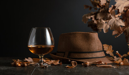 Snifter of brandy on a stone table with dried-up oak leaves.