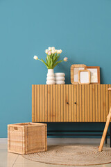 Photo frames and vase with tulips on commode near blue wall in room