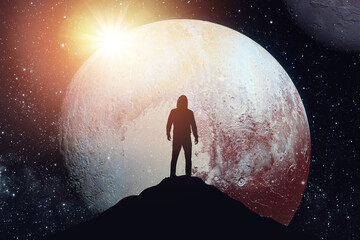 Silhouette of a man standing on the top of a mountain against the backdrop of the planet. Elements of this image furnished by NASA