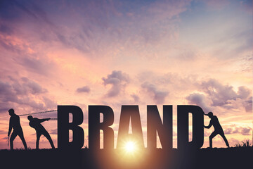 Silhouettes of people drawing the word BRAND on a sunset background, business concept