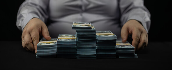 Against a black background, a man folds stacks of hundred dollar bills into neat piles. A lot of...