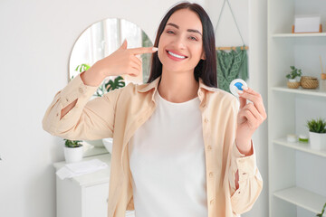 Beautiful young happy woman with dental floss pointing at white teeth in bathroom at home