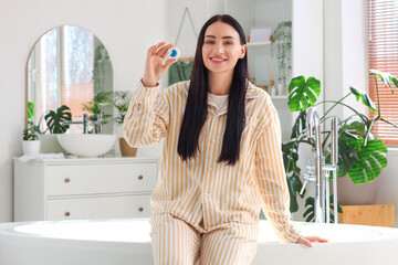 Beautiful young happy woman with dental floss sitting in bathroom at home