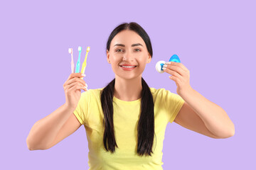 Beautiful young happy woman with different dental floss and toothbrushes on purple background