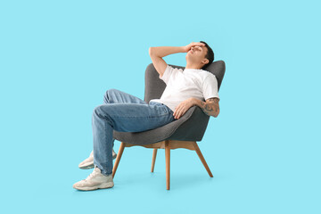 Tired young man sitting in armchair on blue background
