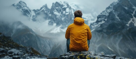 Adventurous man in yellow jacket sits on rocks - Powered by Adobe