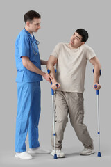 Young man with crutches and doctor on light background. National Cerebral Palsy Awareness Month