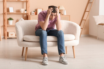Obraz premium Weary young man sitting on sofa at home