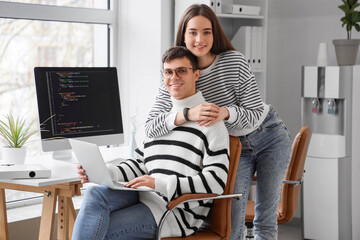 Couple of programmers with laptop hugging in office