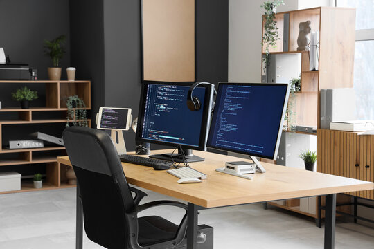 Computer monitors with programming code and headphones on desk in office