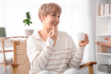 Mature deaf mute woman with cup of coffee and her husband using sign language at home