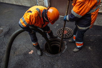 Sewer workers cleaning manhole and unblocking sewers the street sidewalk