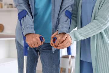 Nurse helping senior man with crutches to walk in kitchen, closeup