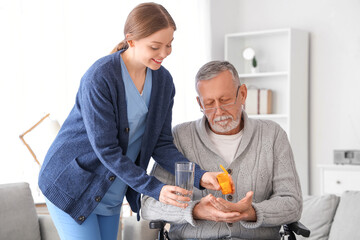Female caregiver giving pills and water to senior man in wheelchair at nursing home