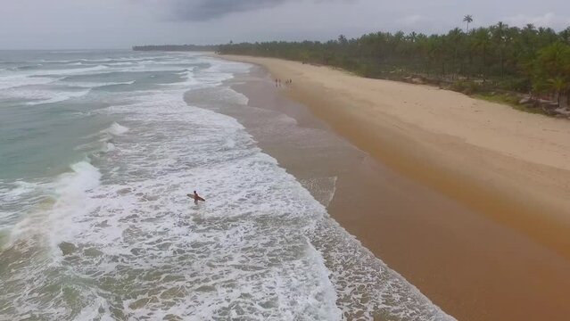 Praia com poucos banhistas em dia nublado. Sobrev&ocirc;o de drone em litoral do nordeste brasileiro em dia feio e chuvoso com surfistas entre as ondas espumosas