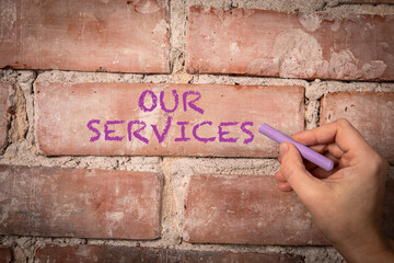 Our Services. Text written with purple chalk on a red brick background