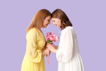 Beautiful mature woman with her daughter holding bouquet of tulips on lilac background. Mother's...