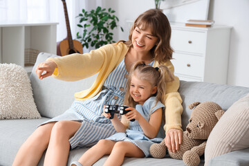Nanny with little girl playing video game on sofa at home
