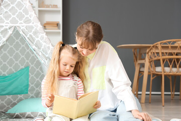 Nanny with little girl reading book at home