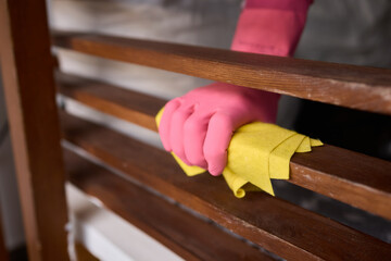 Person in pink gloves cleans wooden table with yellow cloth