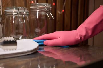Person in pink gloves cleans wooden table with cloth