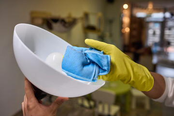 Person in yellow gloves cleans white bowl with blue cloth