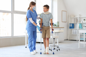 Injured little boy with crutches and doctor walking in clinic