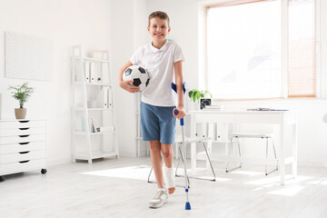 Smiling little boy with crutch and soccer ball in clinic