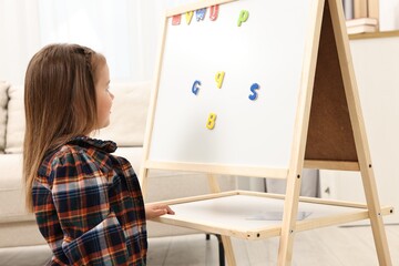 Cute little girl putting magnetic letters on board at home. Learning alphabet