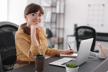 Woman taking notes during webinar at table indoors