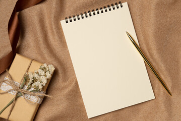 Empty notebook with pen and gift box on a fabric background from above. Copy space