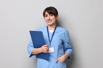 Portrait of smiling medical assistant with clipboard on grey background