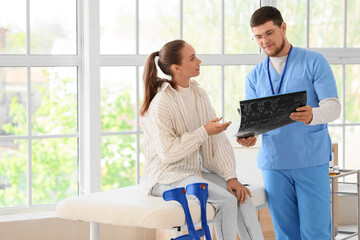 Male doctor showing patient x-ray image of spine in clinic