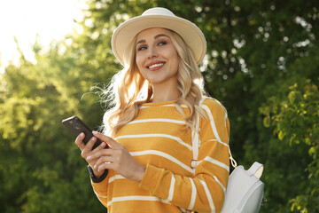 Happy young woman using smartphone in park on spring day