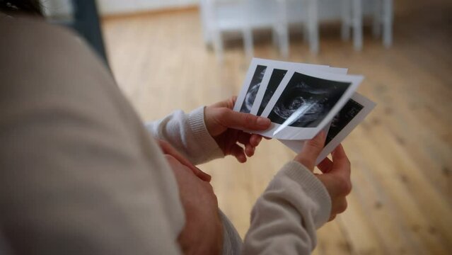 Unrecognizable couple watching ultrasound pregnancy test photo USD pictures indoors at home unknown man pregnant woman girl guy male female parents future mother father family anticipation baby child