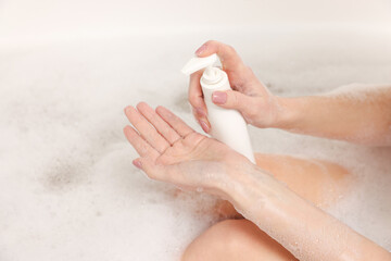 Woman applying shower gel onto hand in bath indoors, closeup
