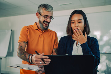 Caucasian businessman showing his work on a laptop to his asian business woman