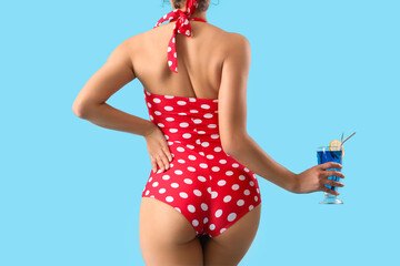 Attractive young woman in polka dot swimsuit with cocktail on blue background, back view © Pixel-Shot