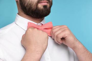 Man in shirt adjusting bow tie on light blue background, closeup
