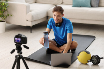 Smiling sports blogger recording fitness lesson with camera at home