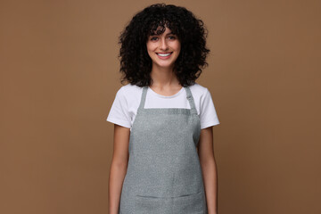 Happy woman wearing kitchen apron on brown background. Mockup for design