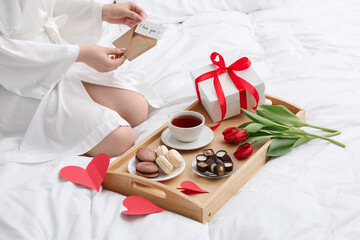 Tasty breakfast served in bed. Woman with I Love You card, desserts, tea, flowers and gift box at home, closeup