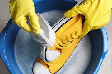 Woman with gloves and brush cleaning stylish sneakers in wash basin, top view