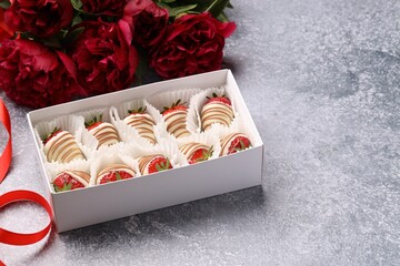 Delicious chocolate covered strawberries in box and flowers on light grey table. Space for text